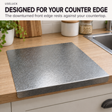 A rectangular gray cutting board with a textured speckled surface and raised edges, shown on a wooden kitchen countertop near a sink. Large text at the top reads 'USELUCK DESIGNED FOR YOUR COUNTER EDGE' with a note about the countertop edge resting against the product.