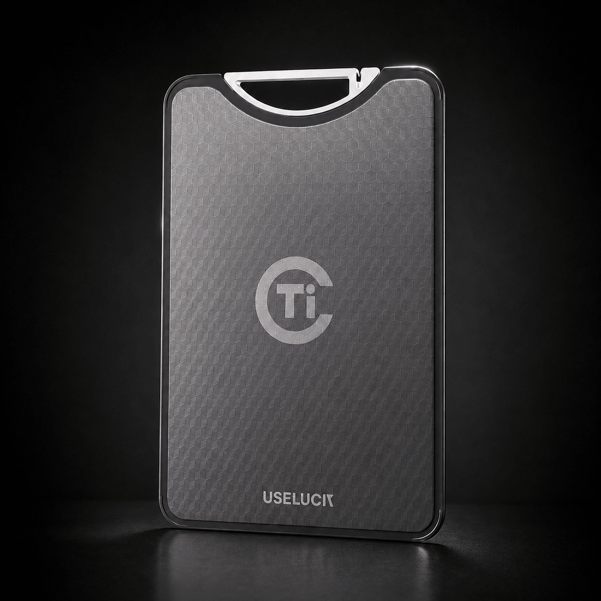 A sleek, rectangular titanium card case with a textured dark gray finish, featuring a silver 'Ti' logo and the brand name 'USELUCI' at the bottom. It is shown standing upright on a dark reflective surface against a black background.