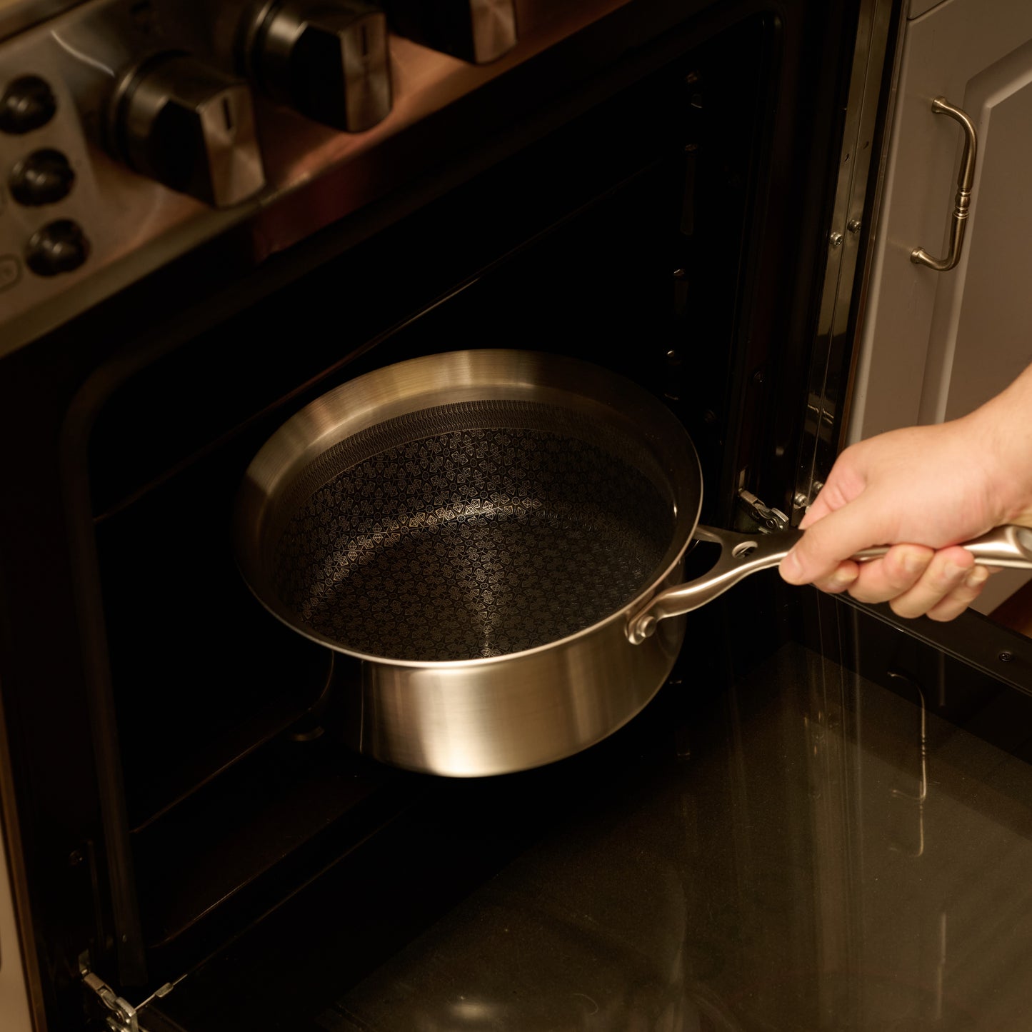 Person holding a stainless steel frying pan over an open oven.